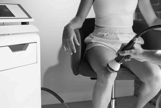 Practitioner applying a therapy applicator to a patient's knee during an in-clinic treatment session
